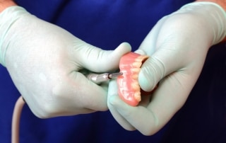 Gloved hands using a tool to fix dentures