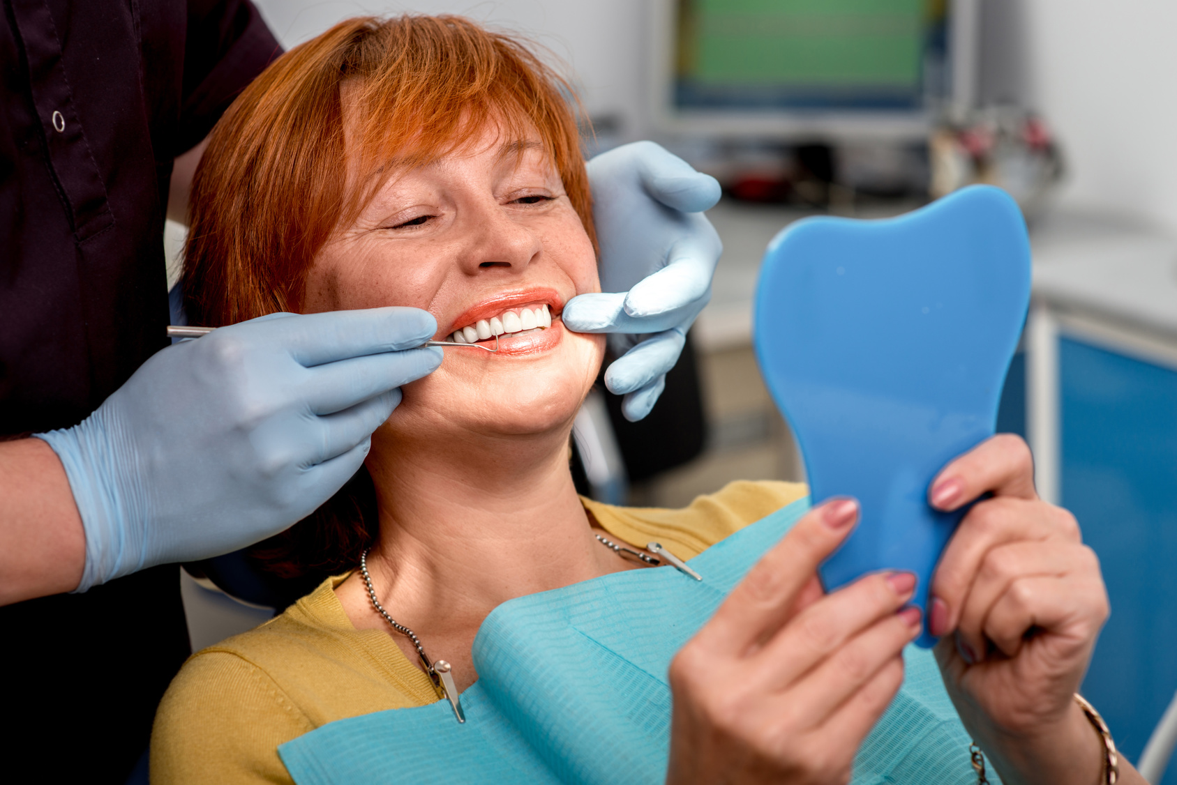 woman in dental chair looking at her smile through a small mirror