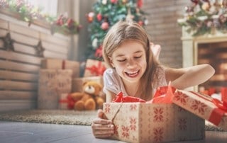 Young girl smiling as she lays on the ground opening a Christmas present