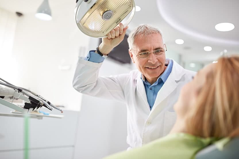 A Dentist adjusts his searchlight before beginning a denture reline procedure to help with a patients bite