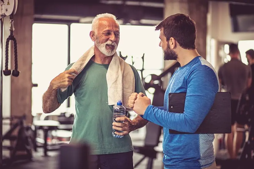 Active senior man finishing his workout at the gym while talking to a friend. With an active lifestyle, he doesn't want implants which is why dentures are his best option. 