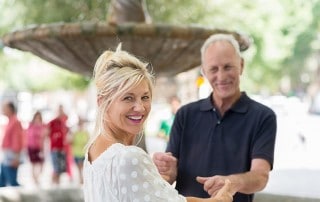 An older couple laughing and spending time with each other outside by a beautiful fountain. You wouldn't know by her smile but her Dentures Don’t Have to Look Like Dentures Anymore!® and they don't have to feel Like Dentures Anymore, Either