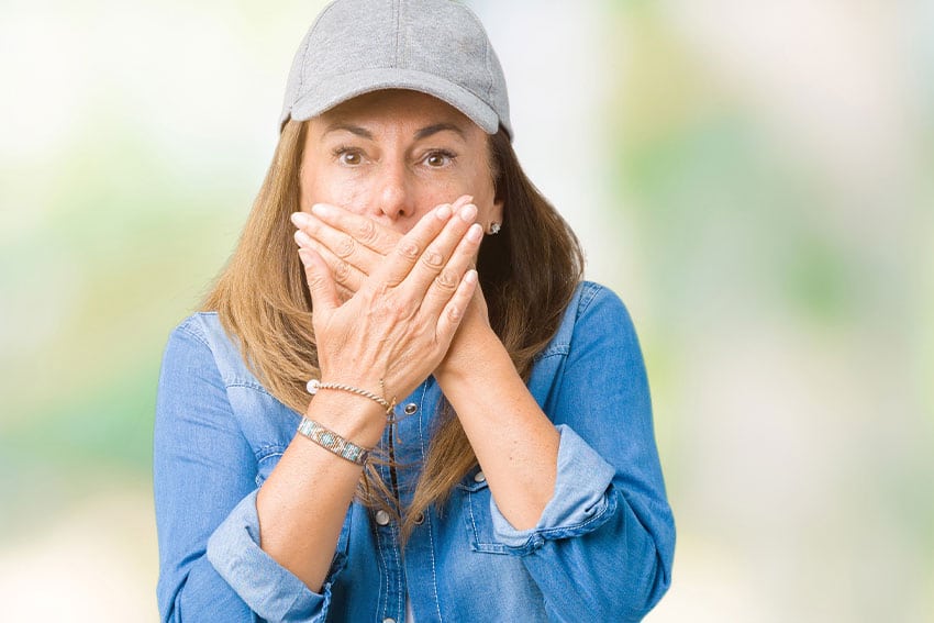 mature woman in baseball hat covering her mouth